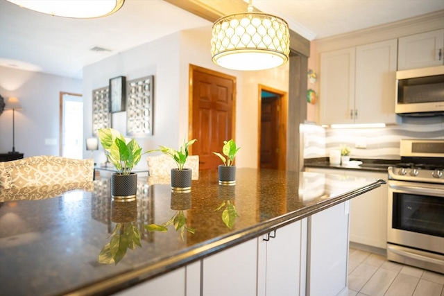 kitchen with decorative light fixtures, dark stone countertops, appliances with stainless steel finishes, and white cabinetry