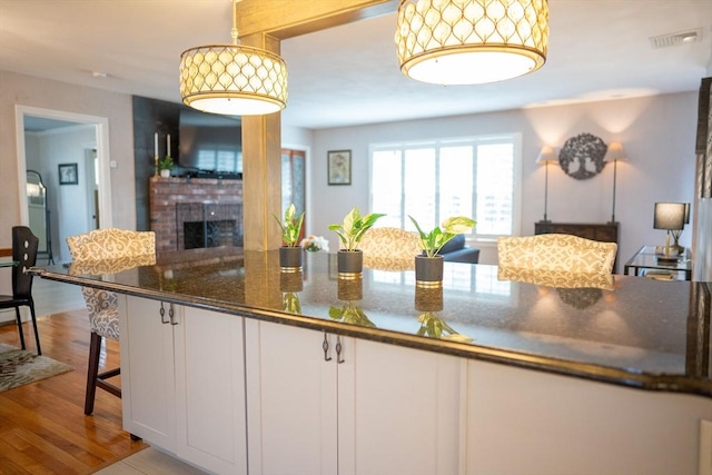 kitchen featuring dark stone countertops, wood finished floors, open floor plan, white cabinetry, and a fireplace