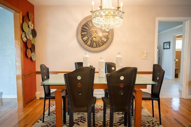 dining space with a chandelier, baseboard heating, baseboards, and wood finished floors