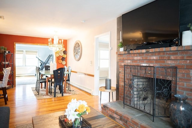 living area featuring a chandelier, a brick fireplace, wood finished floors, and a baseboard radiator