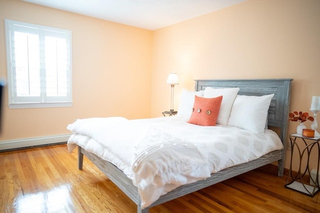 bedroom with a baseboard heating unit, wood finished floors, and baseboards