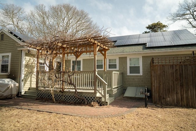 rear view of house featuring a wooden deck, roof mounted solar panels, a pergola, and roof with shingles