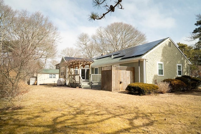 rear view of property featuring a wooden deck, solar panels, and a pergola