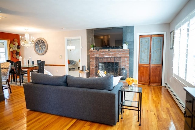 living room featuring a baseboard heating unit, a healthy amount of sunlight, a fireplace, and light wood finished floors