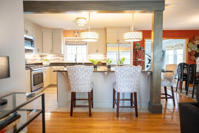 kitchen with a healthy amount of sunlight, light wood finished floors, appliances with stainless steel finishes, dark countertops, and a kitchen breakfast bar