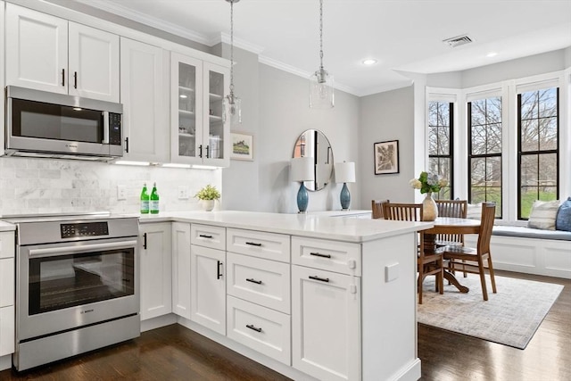 kitchen featuring crown molding, a peninsula, appliances with stainless steel finishes, and dark wood-style flooring