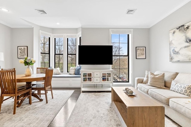 living area with crown molding, wood finished floors, and visible vents