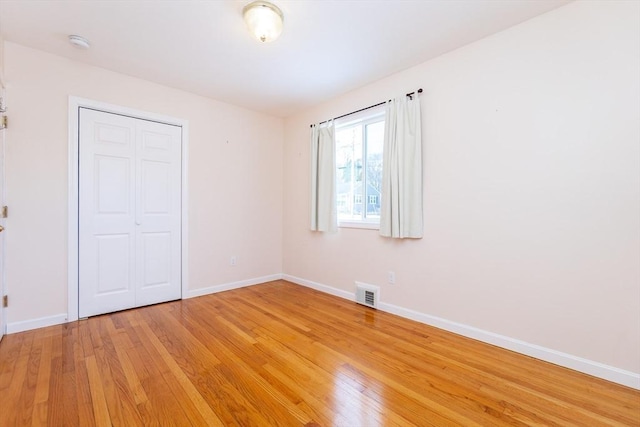 unfurnished bedroom featuring light wood-type flooring, a closet, visible vents, and baseboards