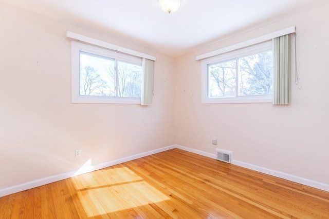 spare room featuring baseboards, plenty of natural light, visible vents, and wood finished floors