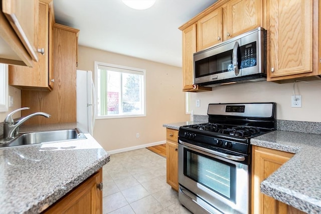 kitchen featuring stainless steel appliances, a sink, light countertops, and baseboards