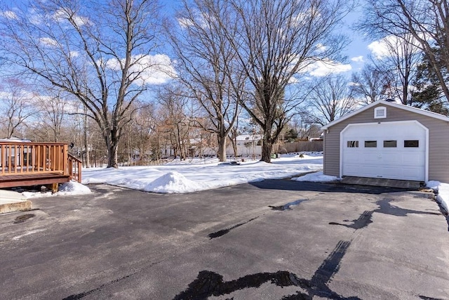 snowy yard with an outbuilding, driveway, a detached garage, and a wooden deck