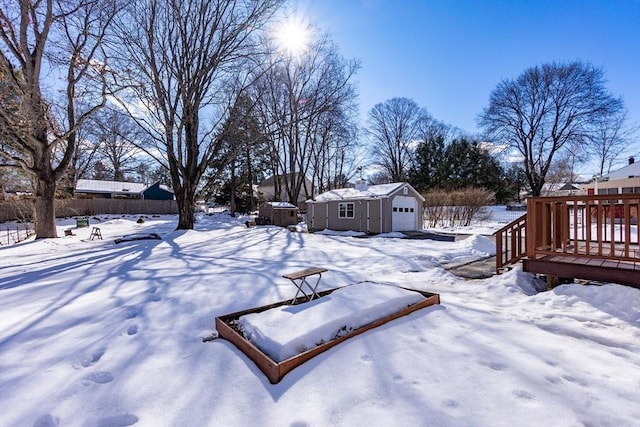 yard covered in snow featuring a garage, fence, a deck, and an outbuilding