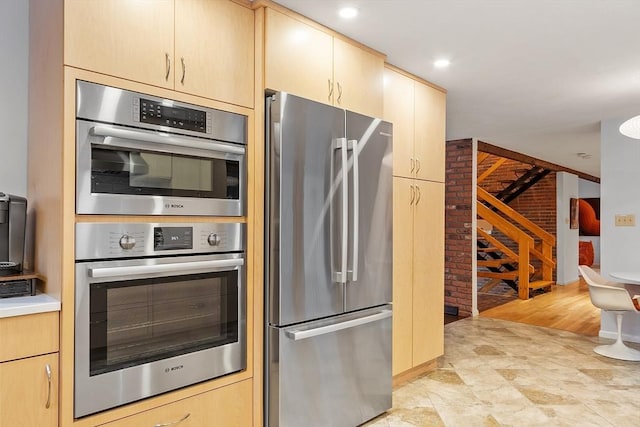 kitchen with light brown cabinetry, stainless steel appliances, and brick wall