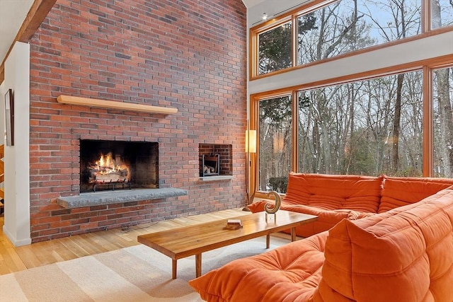 living room with light wood-type flooring, a high ceiling, and a brick fireplace