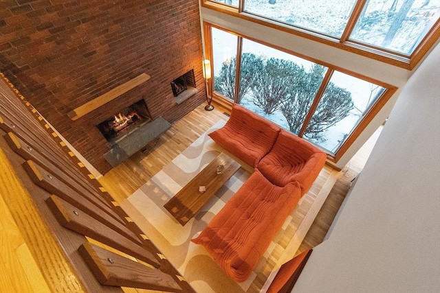 living room with wood-type flooring, a towering ceiling, and a brick fireplace