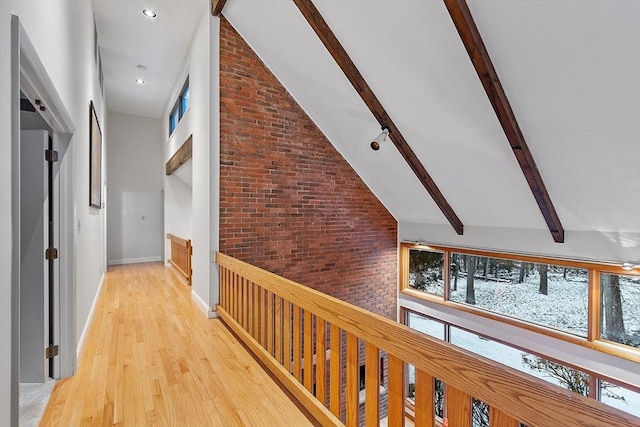 hall with high vaulted ceiling, beamed ceiling, brick wall, and light wood-type flooring