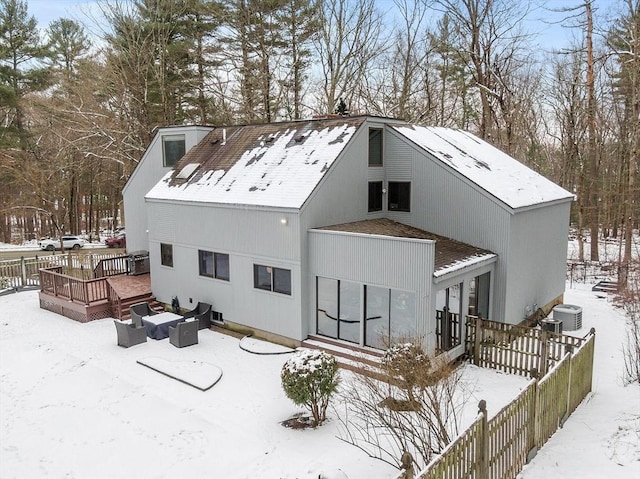 snow covered back of property with central AC and a deck