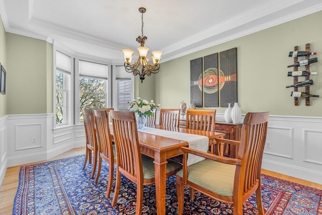 dining area with light wood-type flooring, ornamental molding, wainscoting, and a notable chandelier