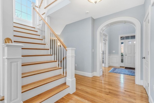 entrance foyer with arched walkways, stairway, and light wood-style floors