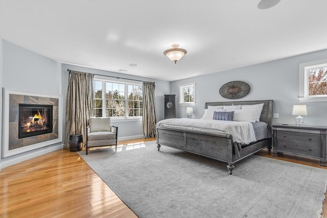 bedroom featuring baseboards, multiple windows, wood finished floors, and a tile fireplace