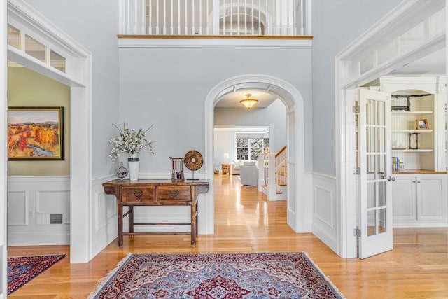 foyer featuring a decorative wall, arched walkways, a wainscoted wall, and light wood-style floors