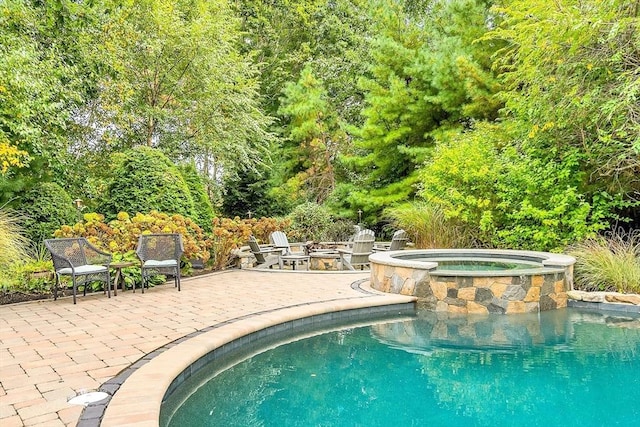 view of swimming pool featuring a pool with connected hot tub, a patio area, and an outdoor fire pit