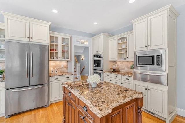 kitchen featuring glass insert cabinets, a warming drawer, light wood-type flooring, appliances with stainless steel finishes, and backsplash
