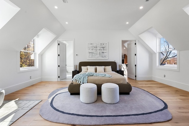 bedroom featuring light hardwood / wood-style floors, ensuite bath, and vaulted ceiling