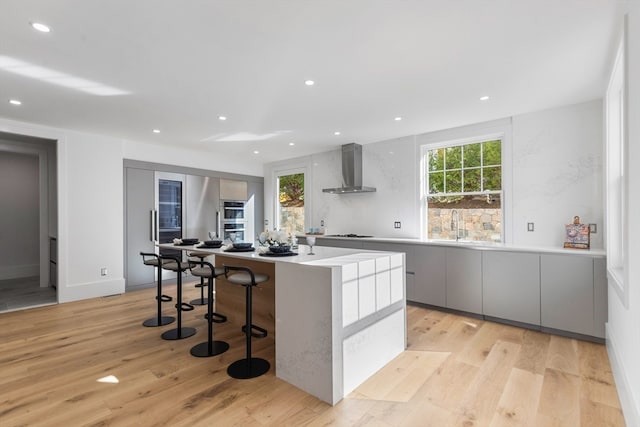 kitchen with light hardwood / wood-style floors, cooktop, wall chimney exhaust hood, a breakfast bar area, and a kitchen island