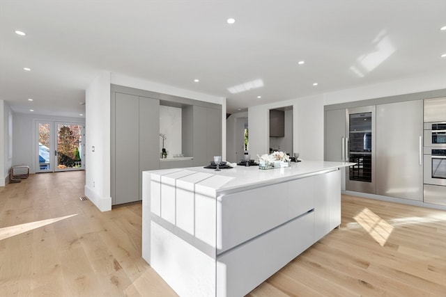 kitchen featuring light wood-type flooring, white cabinets, a spacious island, and double oven