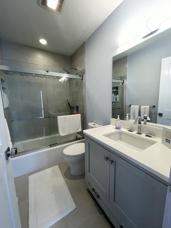 full bathroom with bath / shower combo with glass door, toilet, visible vents, tile patterned floors, and vanity