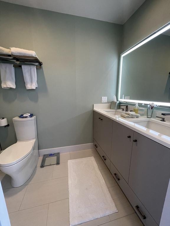 bathroom featuring a sink, toilet, tile patterned floors, double vanity, and baseboards