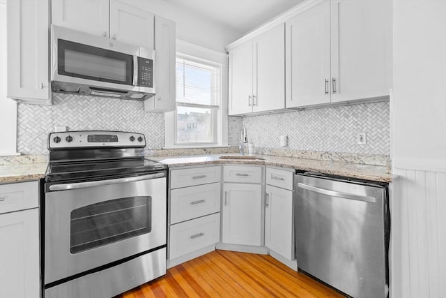 kitchen with stainless steel appliances, sink, white cabinets, and light wood-type flooring