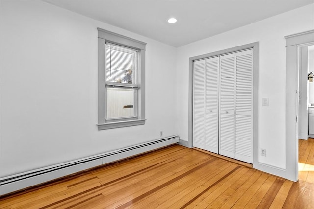 unfurnished bedroom with a baseboard heating unit, wood-type flooring, and a closet