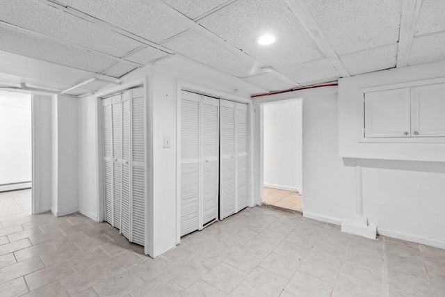 basement featuring a baseboard radiator, light tile patterned floors, and a drop ceiling