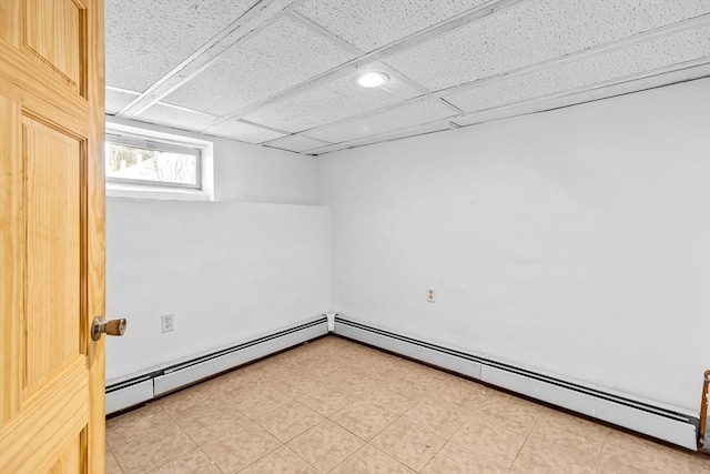 unfurnished room featuring a baseboard heating unit and a drop ceiling