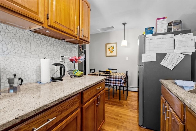 kitchen with pendant lighting, stainless steel refrigerator, decorative backsplash, light stone counters, and light hardwood / wood-style flooring