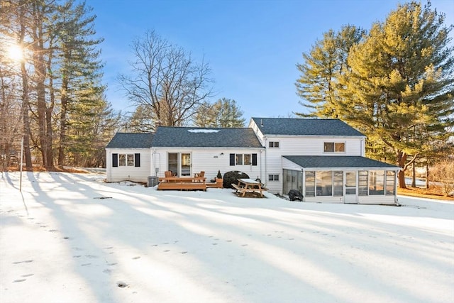 snow covered house with a wooden deck and a sunroom