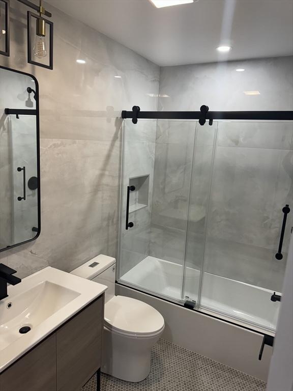 full bathroom featuring tile walls, enclosed tub / shower combo, vanity, toilet, and tile patterned floors