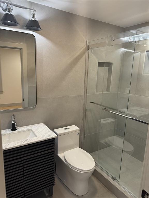 bathroom with vanity, toilet, a shower with shower door, and tile walls