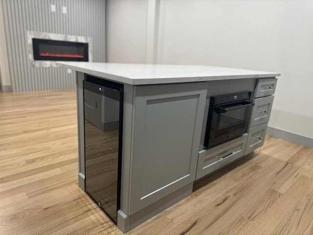 kitchen featuring gray cabinetry, black oven, beverage cooler, and light wood-type flooring