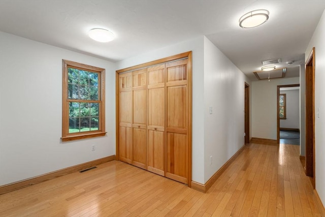 hall with visible vents, attic access, light wood finished floors, and baseboards