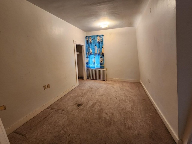 carpeted spare room featuring vaulted ceiling and radiator