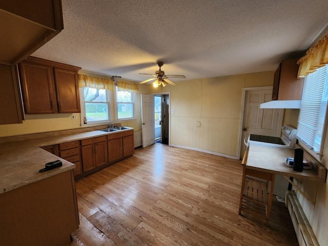 kitchen with a textured ceiling, ceiling fan, a baseboard heating unit, sink, and light hardwood / wood-style flooring