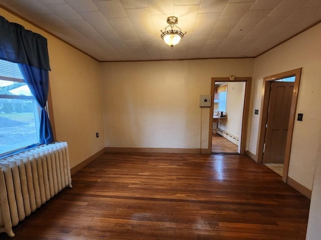 spare room featuring crown molding, radiator heating unit, dark wood-type flooring, and a baseboard heating unit