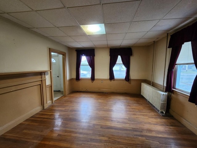 unfurnished room with radiator heating unit, a drop ceiling, and dark hardwood / wood-style floors