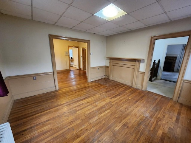 spare room featuring a paneled ceiling, light wood-type flooring, and a brick fireplace