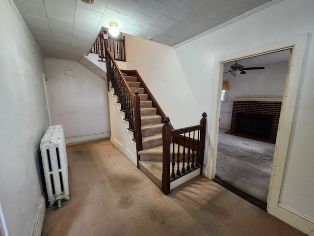 stairway featuring carpet flooring, ceiling fan, radiator heating unit, and a brick fireplace