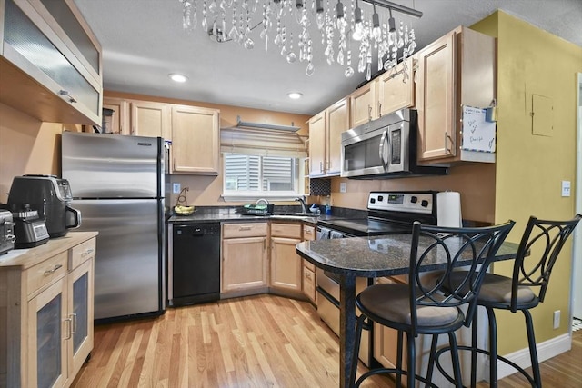 kitchen with a breakfast bar, light brown cabinetry, appliances with stainless steel finishes, decorative light fixtures, and light hardwood / wood-style floors