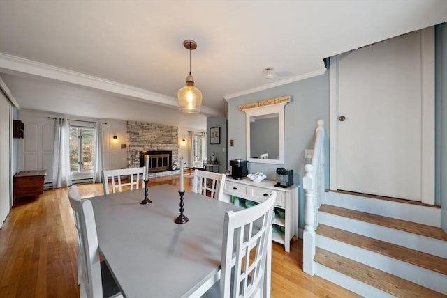 dining space with light hardwood / wood-style flooring, ornamental molding, and a stone fireplace